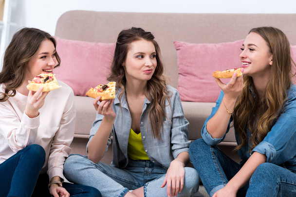 beautiful smiling girlfriends eating pizza and looking at each other - Foto, Imagen