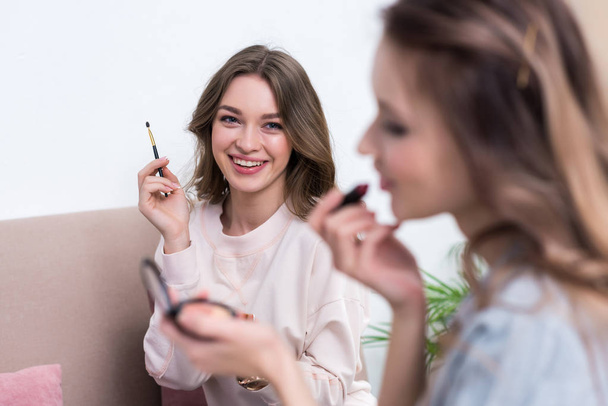 selective focus of smiling young women applying makeup together at home - Foto, imagen