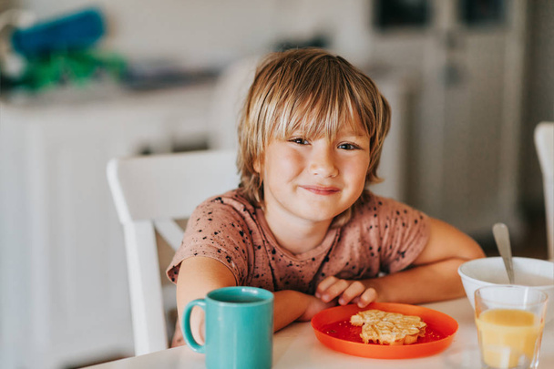 Cute little boy eating his breakfast with waffle and hot chocolate  - Photo, Image