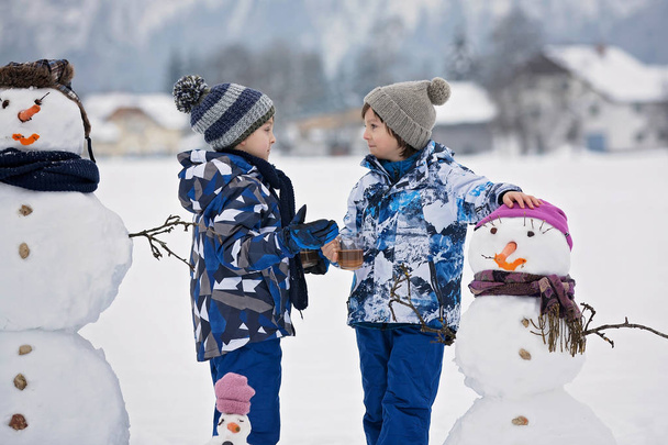 Family with children, building snowman in the park in little vil - Valokuva, kuva