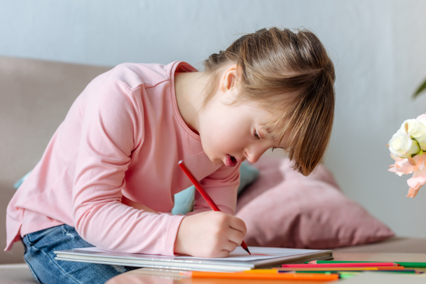Niño con síndrome de Down dibujo entusiasta con lápices de colores
 - Foto, Imagen