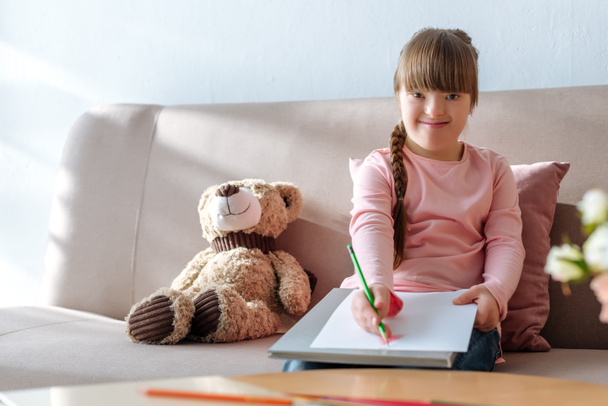 Χαμογελαστό παιδί με σύνδρομο down σχέδιο με χρωματιστά μολύβια - Φωτογραφία, εικόνα