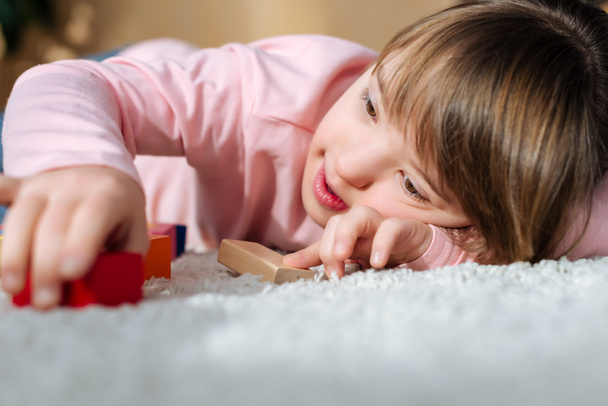 Kind met syndroom van down, spelen met speelgoed kubussen liggend op een vloer - Foto, afbeelding