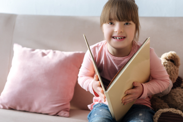 Смеющийся ребенок с синдромом Дауна читает книгу
 - Фото, изображение