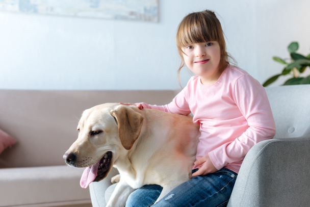 Kid with down syndrome and Labrador retriever sitting in chair - Фото, изображение