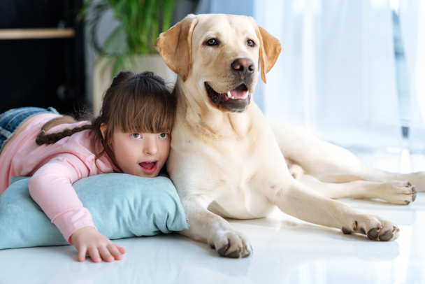 Kid with down syndrome lying on the floor next to Labrador retriever dog - Photo, Image