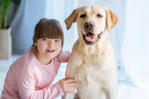 Happy child girl with down syndrome cherishing Labrador retriever  - Фото, изображение