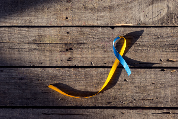 Μπλε και κίτρινη κορδέλα ως σύμβολο της ημέρα για το σύνδρομο Down σε φόντο ξύλινη - Φωτογραφία, εικόνα