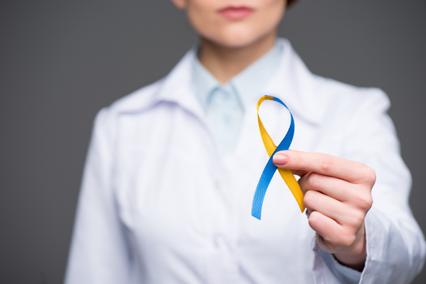 Женщина-врач, держащая синюю и желтую ленточку на день синдрома Дауна, изолирована на сером
 - Фото, изображение