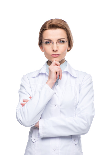 Young smiling female doctor wearing glasses with hand on chin isolated on white - Photo, Image