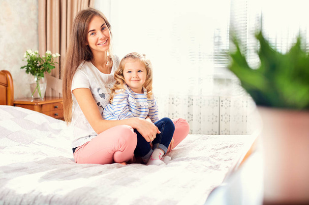 Portrait of mother and daughter on the bed by the window.  - Foto, Bild