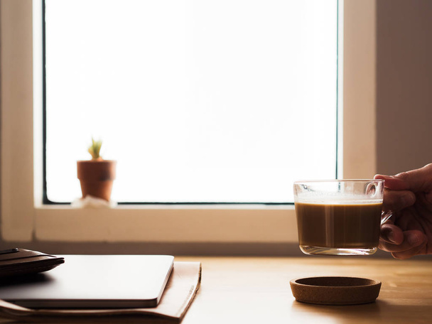 Drinking coffee on workspace desk with laptop by the window ligh - Photo, Image