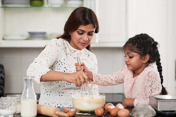 Cute Indian girl helping her beautiful middle-aged mother to beat eggs - Photo, Image