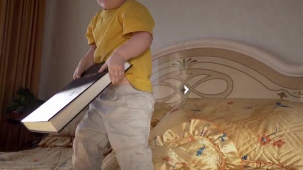 Little Child Sits With Bible On Bed in Bedroom. Opens Book And Turns Pages - Záběry, video