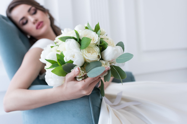 selective focus of bride with wedding bouquet sitting in armchair - Фото, изображение