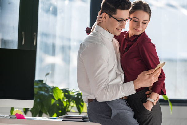 Kollegen umarmen und nutzen gemeinsam Smartphone im Büro - Foto, Bild