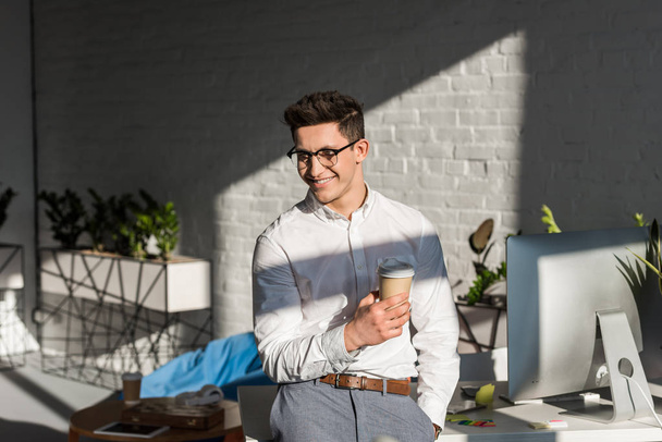 mosolygó fiatal üzletember papír csésze kávé a munkahelyen - Fotó, kép