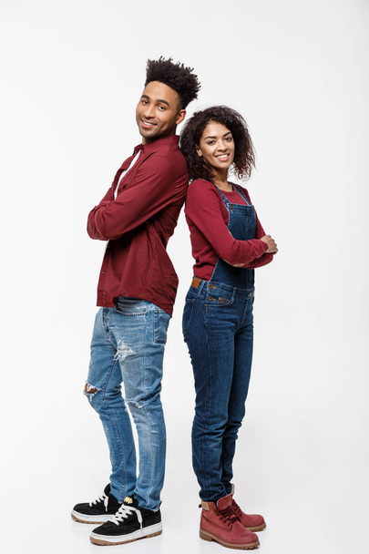 Cheerful African American man and woman with crossed hands standing back to back over isolated white background. - 写真・画像
