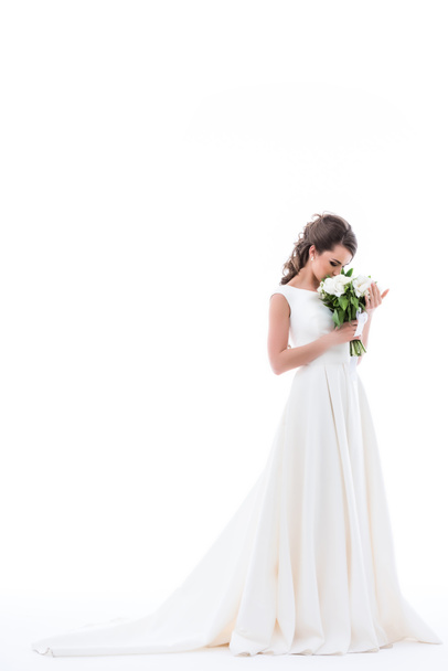 junge Braut im eleganten weißen Kleid schnüffelnd Brautstrauß, isoliert auf weiß - Foto, Bild