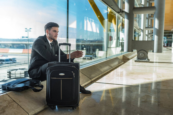 Молодой бизнесмен расстроен в аэропорту ожидая свой задержанный рейс с багажом
 - Фото, изображение