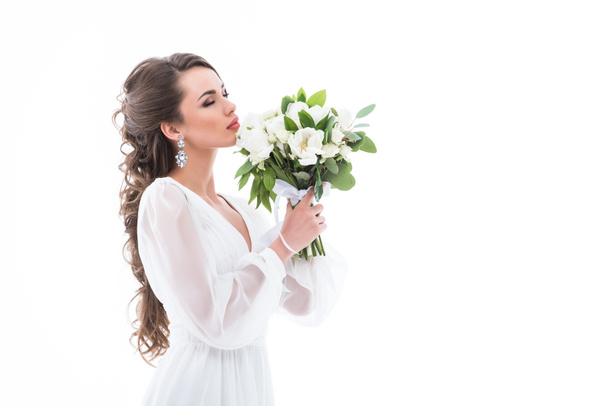 привлекательная невеста в белом платье нюхает свадебный букет, изолированный на белом
 - Фото, изображение