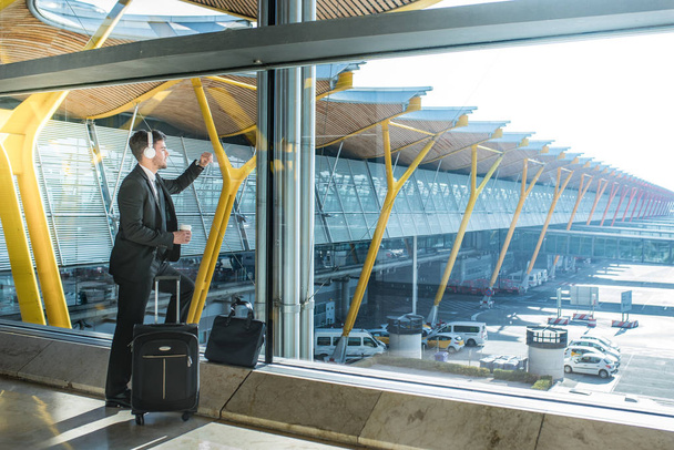 young businessman looking through the window listening music at the airport waiting for his flight - Photo, Image