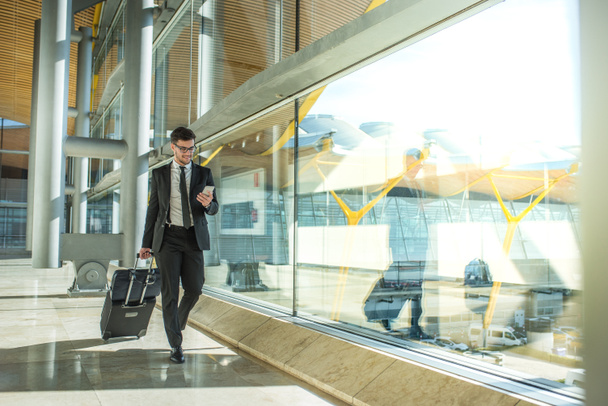 młody biznesmen chodzenie na lotnisku za pomocą swojego telefonu komórkowego - Zdjęcie, obraz