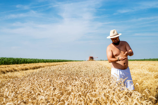 hombre sin camisa con gafas de sol y sombrero de pie en el campo de trigo
  - Foto, imagen