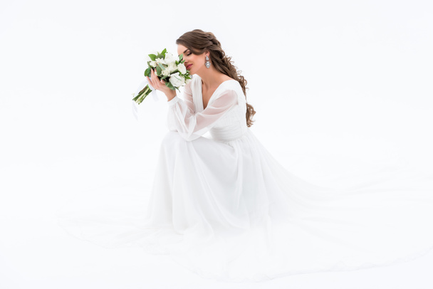 happy bride in traditional dress sniffing wedding bouquet, isolated on white - Foto, Imagem