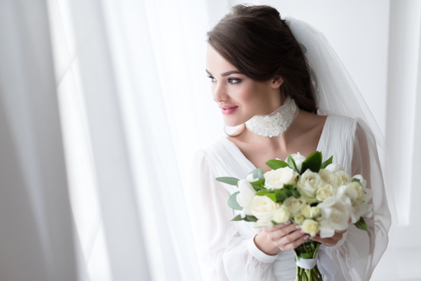 noiva sorridente em vestido de noiva e véu segurando buquê branco
 - Foto, Imagem