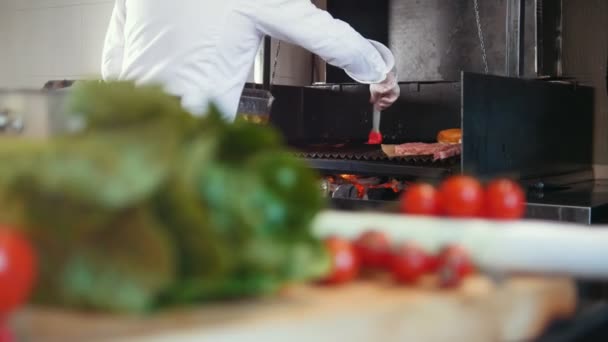 Chef prepara una parrilla para cocinar carne engrasándola con aceite en la cocina comercial, verduras frescas en primer plano
 - Metraje, vídeo