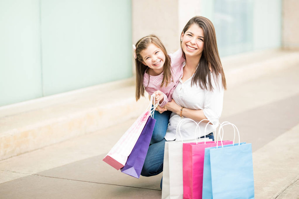 Daughter and mother sitting with colorful bags on storefronts background - Photo, Image