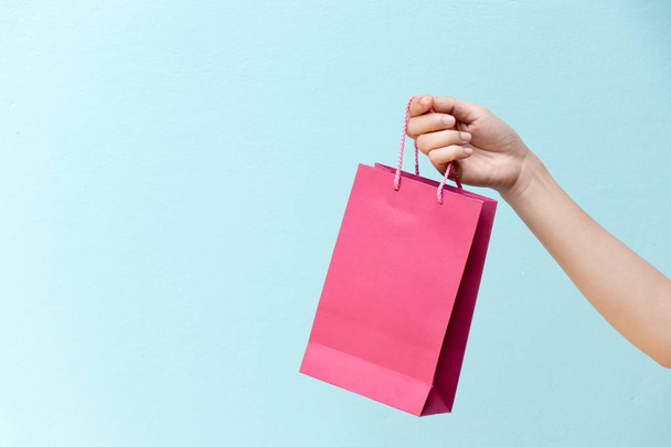 Hand of business woman hold pink shopping bag on blue concrete background - Φωτογραφία, εικόνα