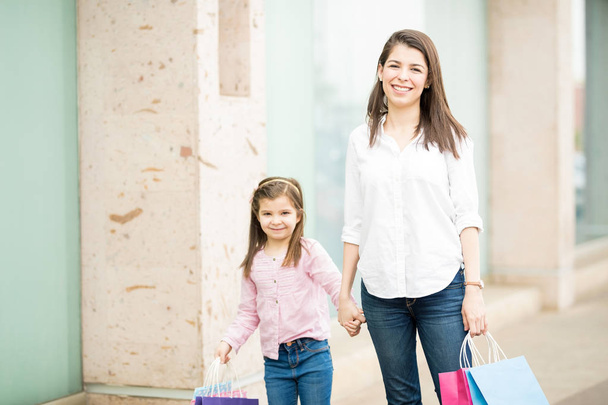 Vitrin camekanlar arka plan üzerinde renkli alışveriş torbaları ile anne ve kızı ayakta - Fotoğraf, Görsel