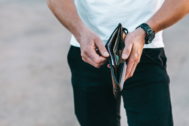 Young caucasian man in white t-shirt holds wallet in hands - Φωτογραφία, εικόνα