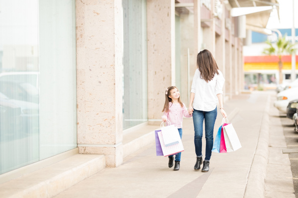 Dochter en moeder in volle lengte wandelen met kleurrijke tassen langs storefronts  - Foto, afbeelding