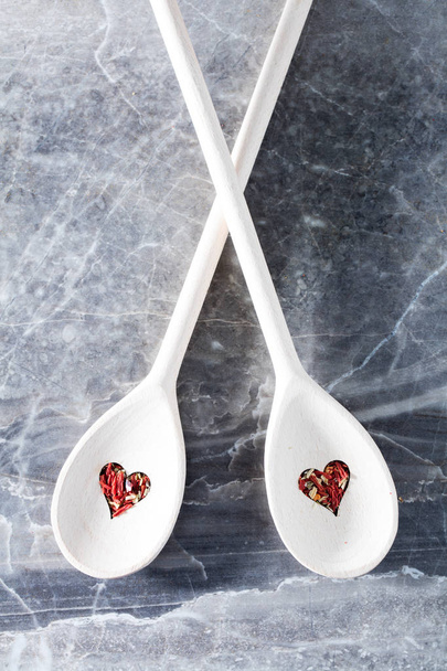 Twee houten lepels met hartvormige gaten en droge chili kruiden opleggen van een teller. - Foto, afbeelding