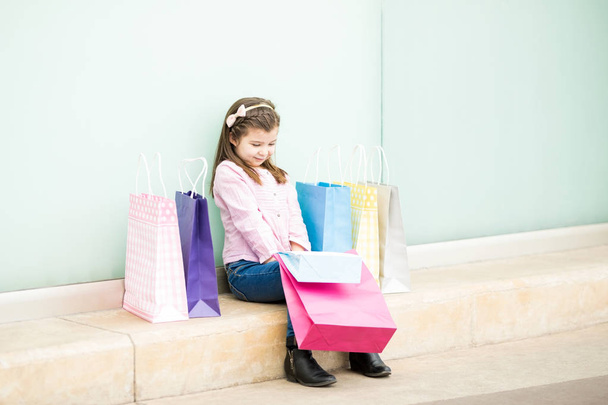 カラフルなショッピング バッグを店舗近くに座って女の子 - 写真・画像