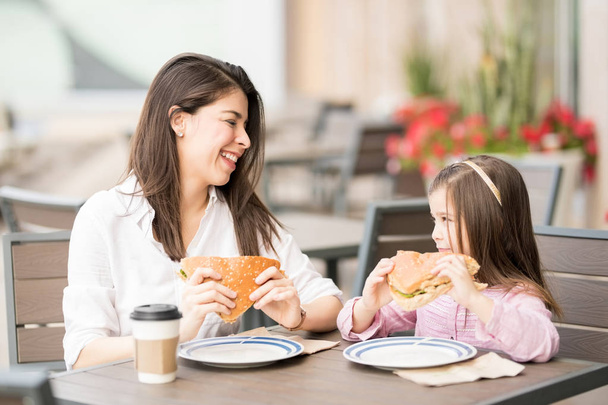 Мати і дочка посміхаються і їдять бургер в кафе
  - Фото, зображення