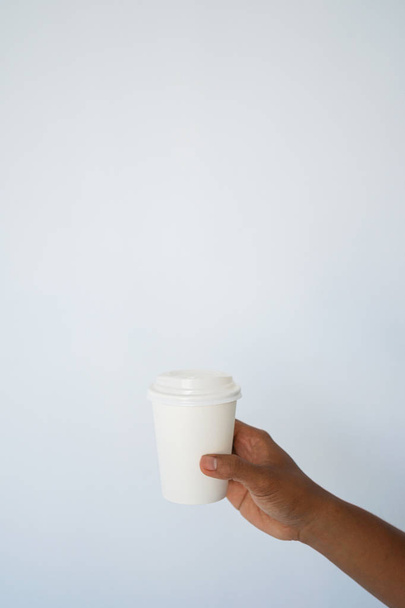 Ręka mężczyzny ciemnoskórych posiada jednorazowego kubka do kawy lub herbaty tło białe i niebieskie ściany. Widok z boku z miejsca kopii - Zdjęcie, obraz