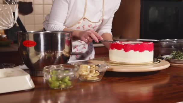 Mulher cozinheiro está aplicando uma cor vermelha creme cremoso em um bolo em uma cozinha
 - Filmagem, Vídeo