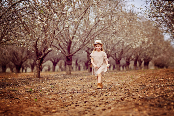 Girl in a neglected almond orchard. Girl in white running along old almond garden - Foto, Bild