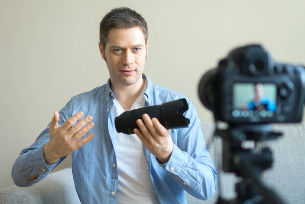 ハンサムな男が写真カメラのレンズについてのビデオブログを作る. - 写真・画像
