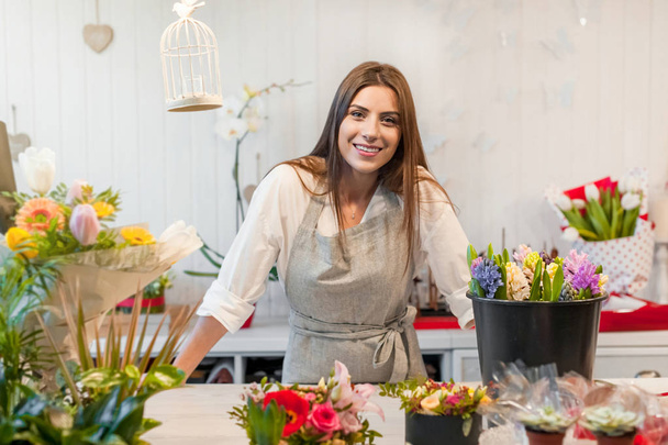 Усміхнена жінка-флорист малого бізнесу власник квіткового магазину, за стійкою, виглядає доброзичливо на камеру
. - Фото, зображення