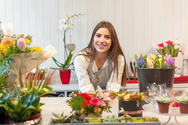 Усміхнена жінка-флорист малого бізнесу власник квіткового магазину, за прилавком, змалку дивиться на камеру
. - Фото, зображення