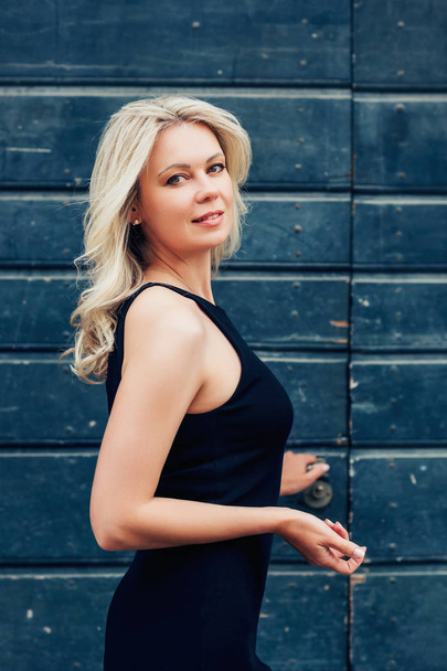 Outdoor portrait of young blond woman wearing black dress - Photo, Image