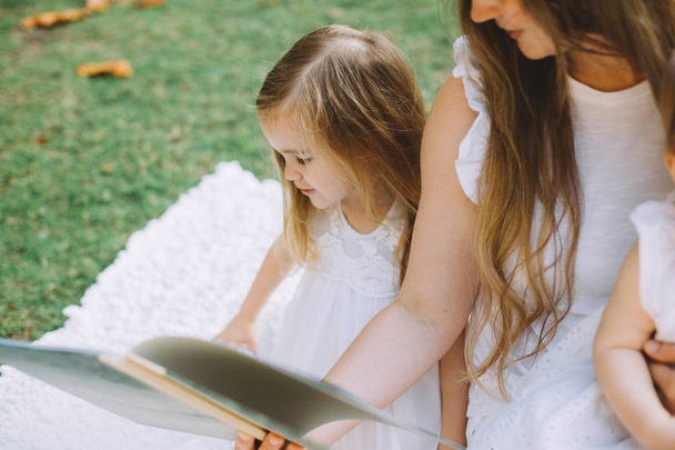madre leyendo libro en el picnic de verano en el parque a sus hijas
 - Foto, Imagen
