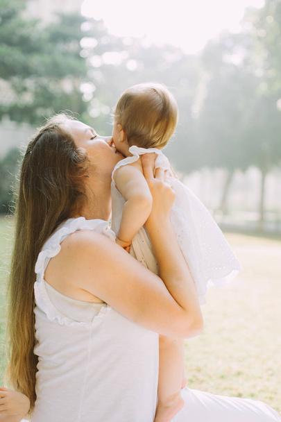 портрет щасливої красивої молодої матері цілує свою чарівну маленьку доньку, сімейний пікнік влітку
 - Фото, зображення