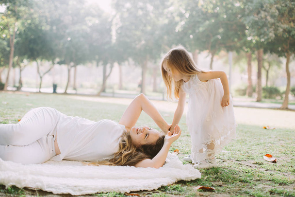 Porträt der schönen jungen Mutter, die mit ihrer entzückenden kleinen Tochter im Park spielt - Foto, Bild