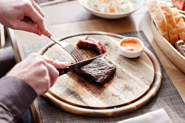 the man in the restaurant with a knife cuts steak of marble beef, grilled. Serving on a wooden Board. - Foto, imagen